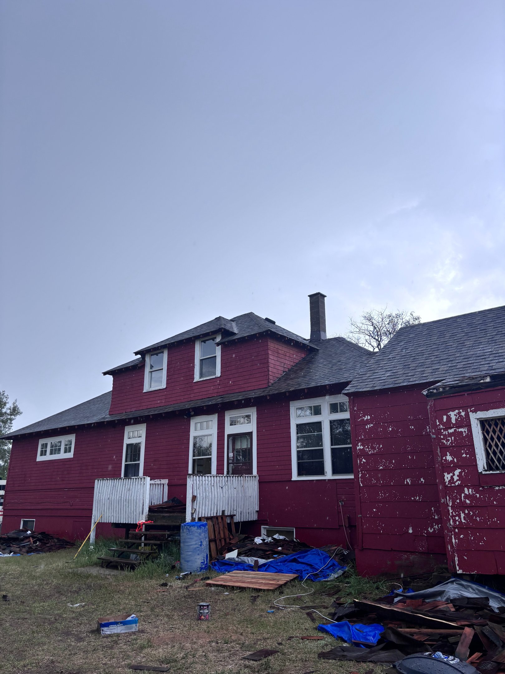 Red two-story house getting a full roof replacement by the No Stress Roofing crew