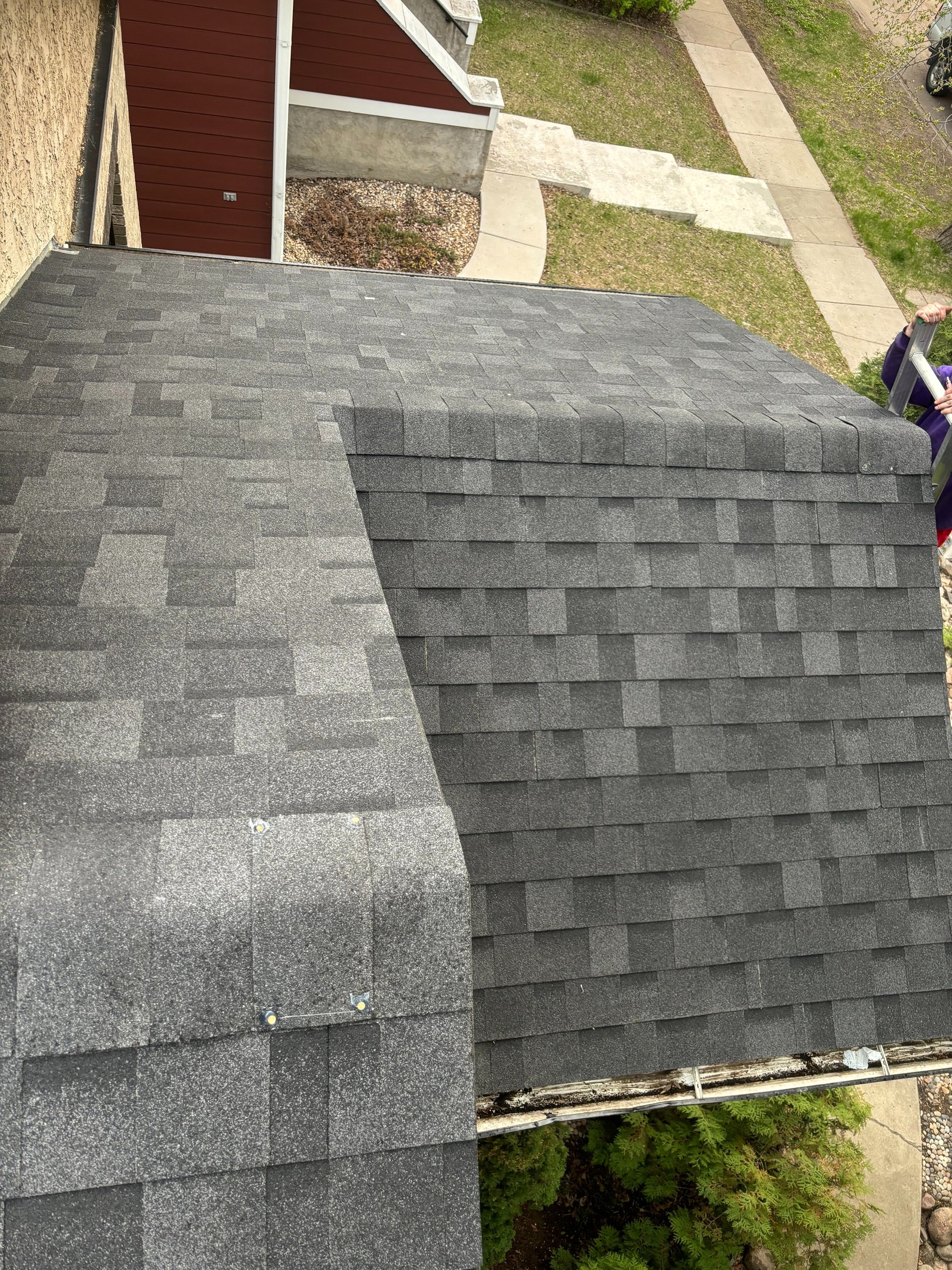 No Stress Roofing roofer finishing a dark shingle roof edge from a ladder